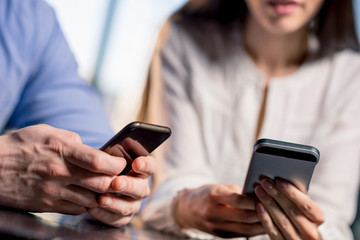 Close-up partial view of young couple using smartphones together, lunch meeting concept