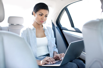Fototapeta na wymiar concentrated african american woman working with laptop in taxi