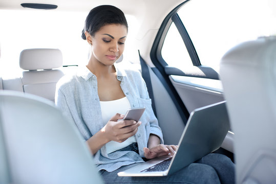 Concentrated African American Woman Working With Laptop And Smartphone In Taxi