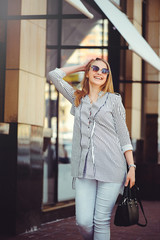 Young happy woman laughs walking around the city wearing glasses and with a handbag, modern coins