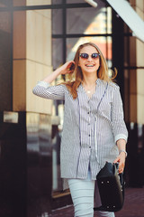 Young happy woman laughs walking around the city wearing glasses and with a handbag, modern coins