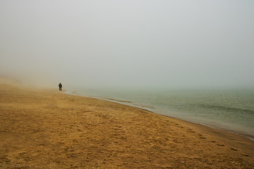 Obraz premium The old man and the sea. Silhouette of an old man with a cane walking on a foggy beach. Minimalist concept.