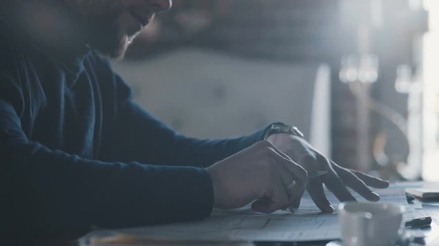 esign of the house. Engineer. Tools for drawing. Creating a drawing. Architecture.Pensive young handsome man writing in his notebook while sitting at his working place. Drawings, design project and