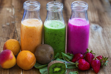 Fresh healthy three types of fruits juices or smoothies bottles, orange, green and pink with strawberries, apricots and kiwi