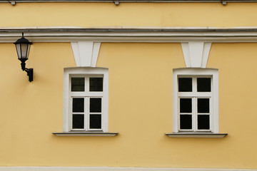 The facade of two windows of a yellow building and an old lantern on it.