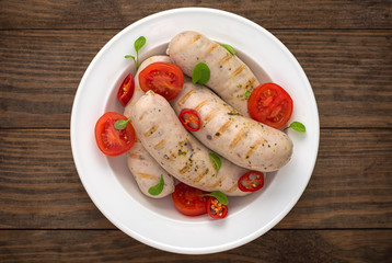 Boiled grilled sausages with cherry tomatoes and chili peppers with greens. Wooden background. Top view. Close-up