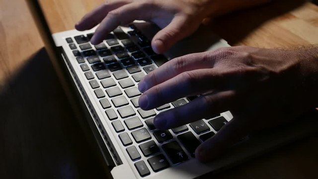 Man typing on laptop keyboard, late night, side angle