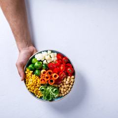 Raw mixed Vegetables and chickpeas on a white. Background Vegetarian Buddha Bowl in the Men's Hands. Food or Healthy diet Concept.Super Food.Copy space for Text. selective focus.