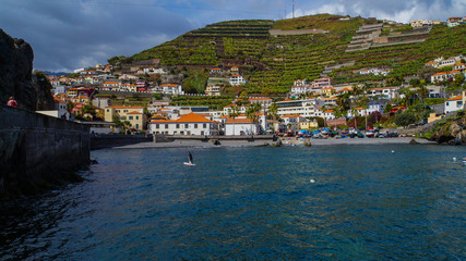 Fototapeta na wymiar Madeira - Village of Camara de Lobos from the ocean with paddler in the water and green banana plants