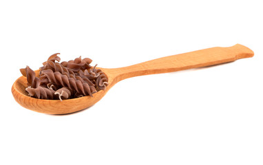 Dark raw fusilli pasta in spoon on white background