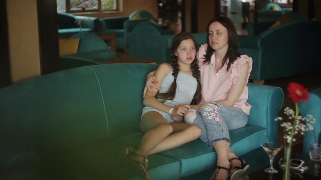 Family holiday. A woman and her daughter are sitting on a turquoise sofa in a cafe and talking to each other