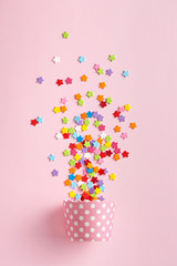 Celebration concept. Cupcake paper cup with colorful stars on a pink background. Top view