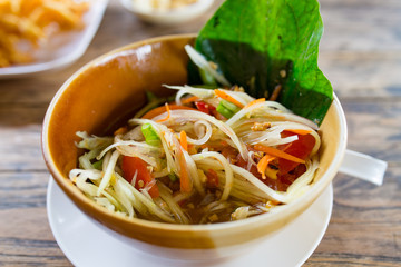 partial and soft focus of green papaya salad in brown bowl on wooden background