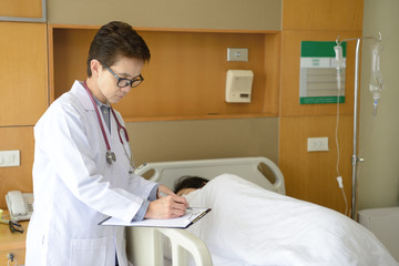 Female  doctor writing on a medical chart with patient lying in a hospital bed