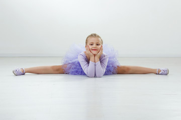 beautiful blond caucasian young girl in lilac dress doing stretching exercises at ballet school