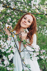 Red-haired girl with freckles near the apple tree