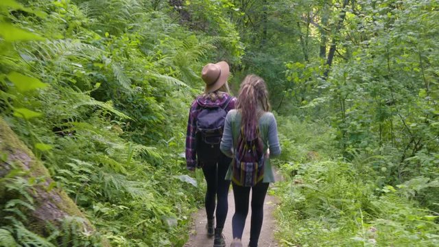 Hikers Walk (Away From Camera) Down Trail, Curious Woman Touches Plants Along The Way