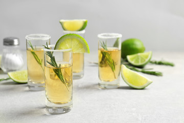 Golden tequila shots with juicy lime slices, rosemary and salt on light background
