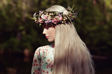 Beautiful blonde woman with flower wreath on her head. Beauty girl with flowers hairstyle. Girl in a summer forest. Fashion photo