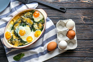Baking dish with delicious cooked eggs Florentine and napkin on wooden background