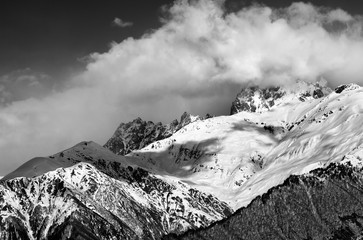 Black and white view on snow mountains in clouds in winter sun day