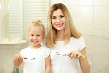 Happy little girl with her mother brushing teeth in bathroom