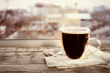 Glass cup of delicious hot coffee on wooden window sill