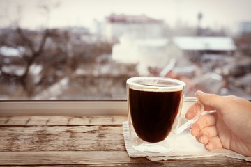 Human hand taking cup of hot coffee from wooden window sill