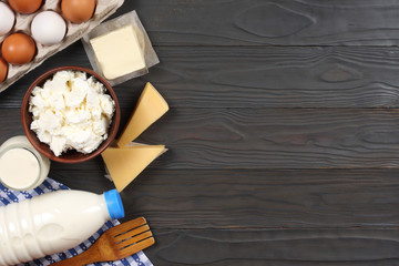 Glass jug pitcher of fresh milk with glass, eggs and cottage cheese in a rustic setting on the wooden background  with copy space. Top view.