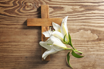 Wooden cross and white lily on table