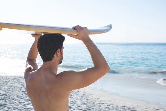 Rear view of shirtless man carrying surfboard at beach