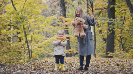 Little daughter with her mother and Teddy Bear walking in autumn park