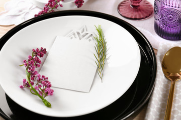 Table setting with cream color napkin, blank card and lilac floral decor on wooden surface