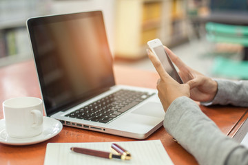 woman's hands using smartphone and laptop in to working on table