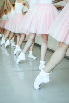 The close-up feet of a three young ballerinas in pointe shoes against the background of the wooden floor