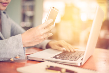 woman's hands using smartphone and laptop in to working on table