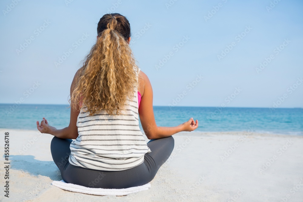 Wall mural rear view of young woman meditating on sand at beach