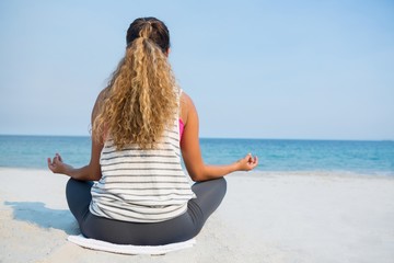 Fototapeta na wymiar Rear view of young woman meditating on sand at beach