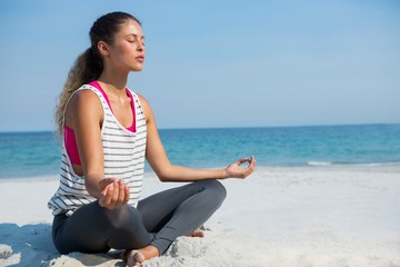 Fototapeta na wymiar Full length of young woman meditating at beach