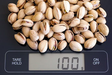 Roasted and salted pistachios on digital scale  displaying 100 gram