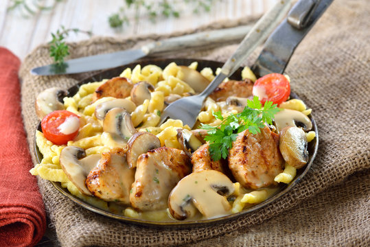 Deftiges Schwabenpfandl mit Schweinemedaillons und Sp&auml;tzle mit Pilzrahmso&szlig;e in der Eisenpfanne serviert - Fried pork fillet with Swabian spaetzle and mushroom cream sauce served in an iron frying pan