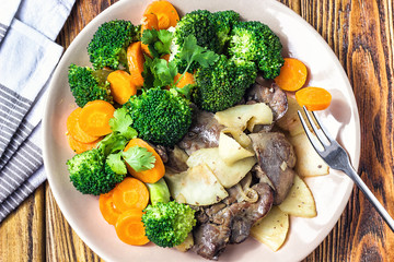 Fried chicken liver with vegetables apples broccoli carrots onions and herbs on a dish on the wooden table, horizontal view from above. Top view of tasty food.