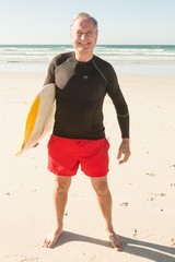 Portrait of man carrying surfboard while standing on sand