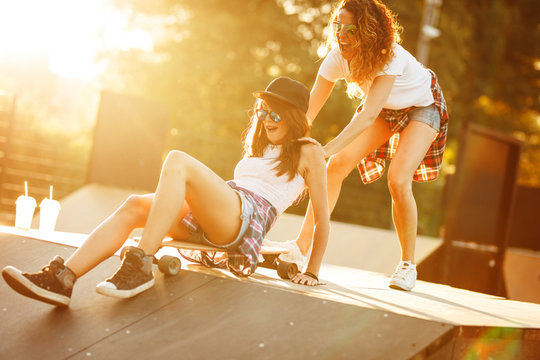 Two female friends playing with skateboard at the skate park.One girl pushing other from behind.Laughing and fun.