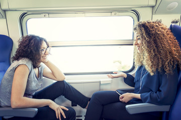 two smiling lovely girls talk to each other sitting in a carriage train