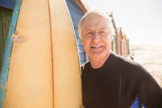 Portrait Of Senior Man Standing By Surfboard