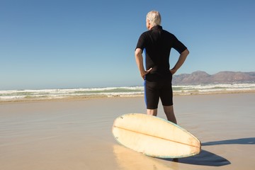 Rear view of man standing by surfboard against clear sky