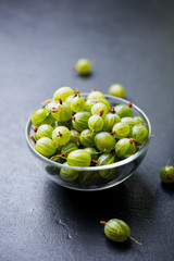 Fresh gooseberries in glass bowl on black stone slate background.