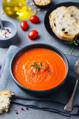 Tomato soup in a black bowl on grey stone background.