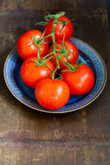 Tomatoes on the twig, dark blue plate. Isolated. Wooden background background.